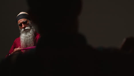 Close-Up-Low-Key-Studio-Lighting-Shot-Of-Two-Sikh-Men-Folding-Fabric-For-Turban-Against-Plain-Background